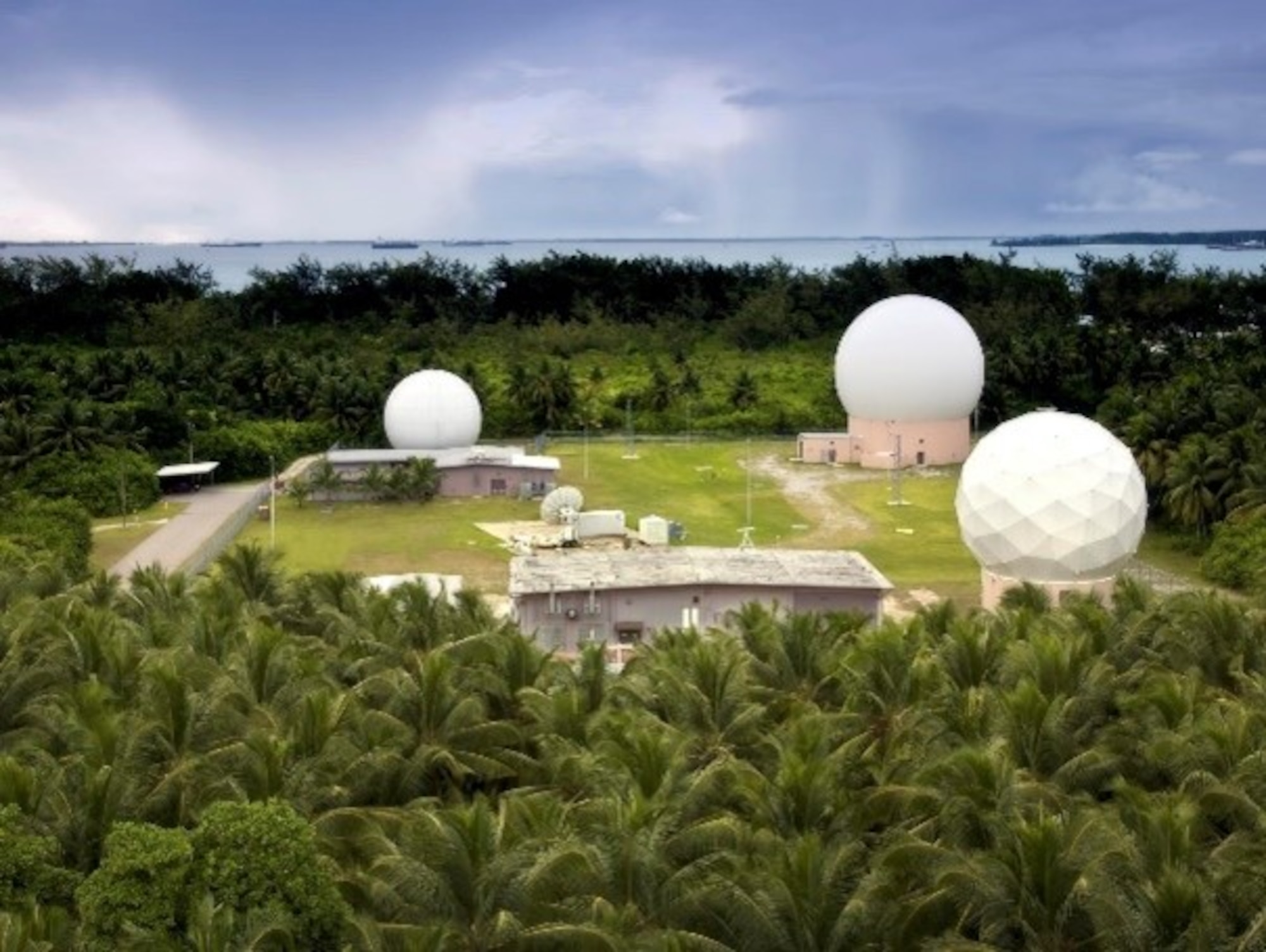 A photo of tropical landscape of Diego Garcia with an open field with facilities and three radomes.