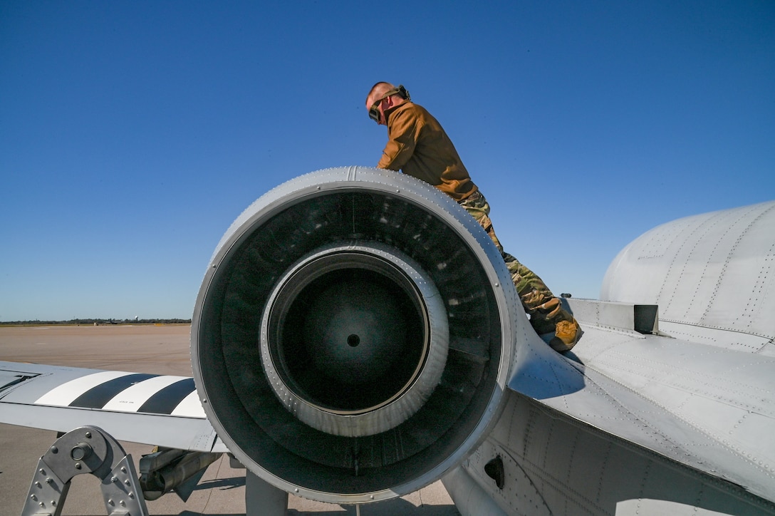 An airman leans over the propeller and wing of a military aircraft during an inspection.
