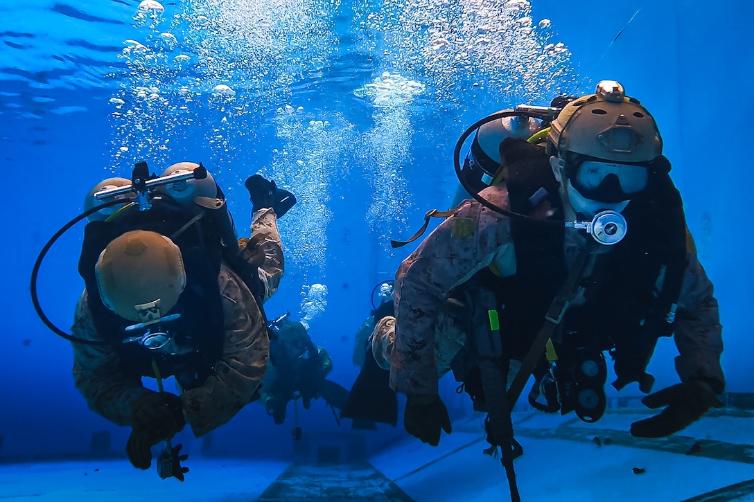 Two uniformed Marines wear dive gear during underwater training.