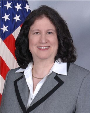 Photographic headshot of professionally dressed person in front of American Flag background.