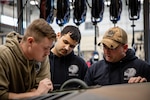 (From left to right) Oklahoma Army National Guardsmen Sgt. Kyle Ehrenberg, a rocket system crewmember assigned to the 1st Battalion, 158th Field Artillery Regiment, 45th Field Artillery Brigade, Spc. Jasser Reyes, a wheeled vehicle mechanic assigned to the 120th Forward Support Company, 45th FAB, and Staff Sgt. Brandon Burns, a motor transport operator assigned to the 120th FSC, 45th FAB, read instructions together during the Mechanic of the Year competition held at the Combined Support Maintenance Shop in Norman, Oklahoma, Feb. 7, 2024. The Guardsmen gathered to put their mechanic skills to the test in the third annual competition, working in four-man teams to beat out the competition while also getting to network amongst fellow competitors. (Oklahoma National Guard photo by Cpl. Danielle Rayon)