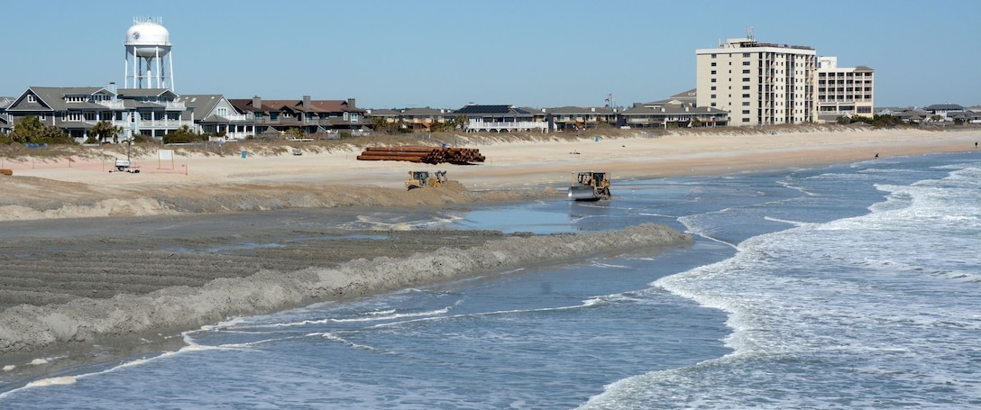 A bulldozer moving sand on a beach by the ocean.