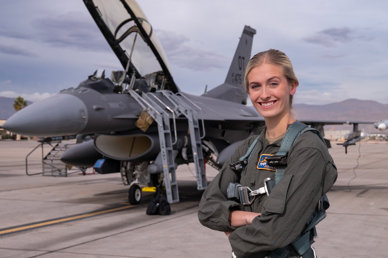 A woman poses in front of a fighter aircraft on tarmac.