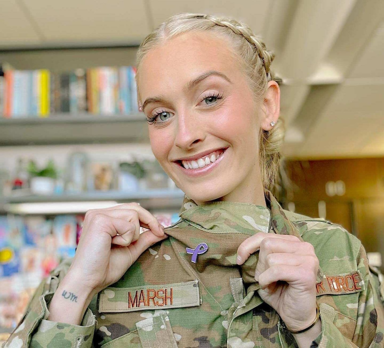 A smiling woman shows off a purple ribbon pin on her uniform.