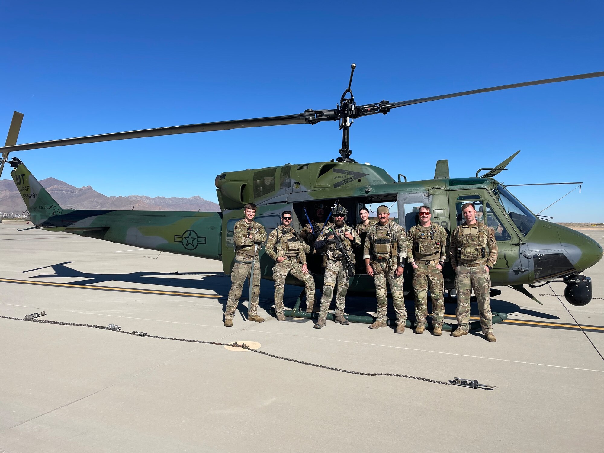 A group of Air Force members - some with helmets and weapons - stand in front of a green helicopter.