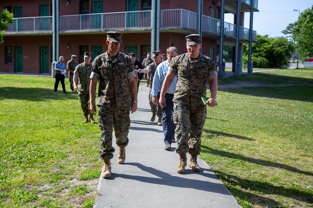 Marines in uniform walking on a sidewalk in front of a barracks building.