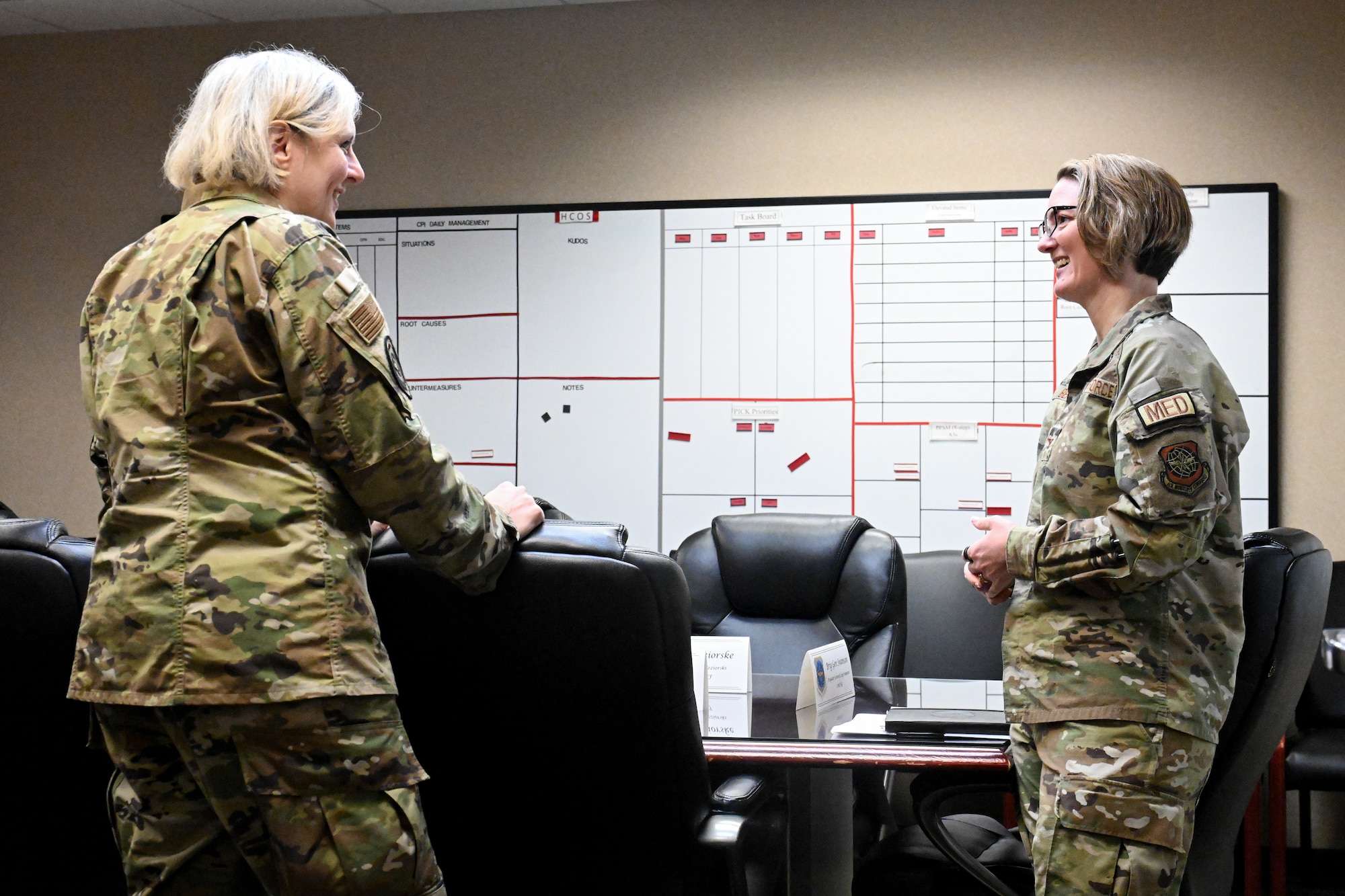Two Airmen stand and talk in a medical building conference room.