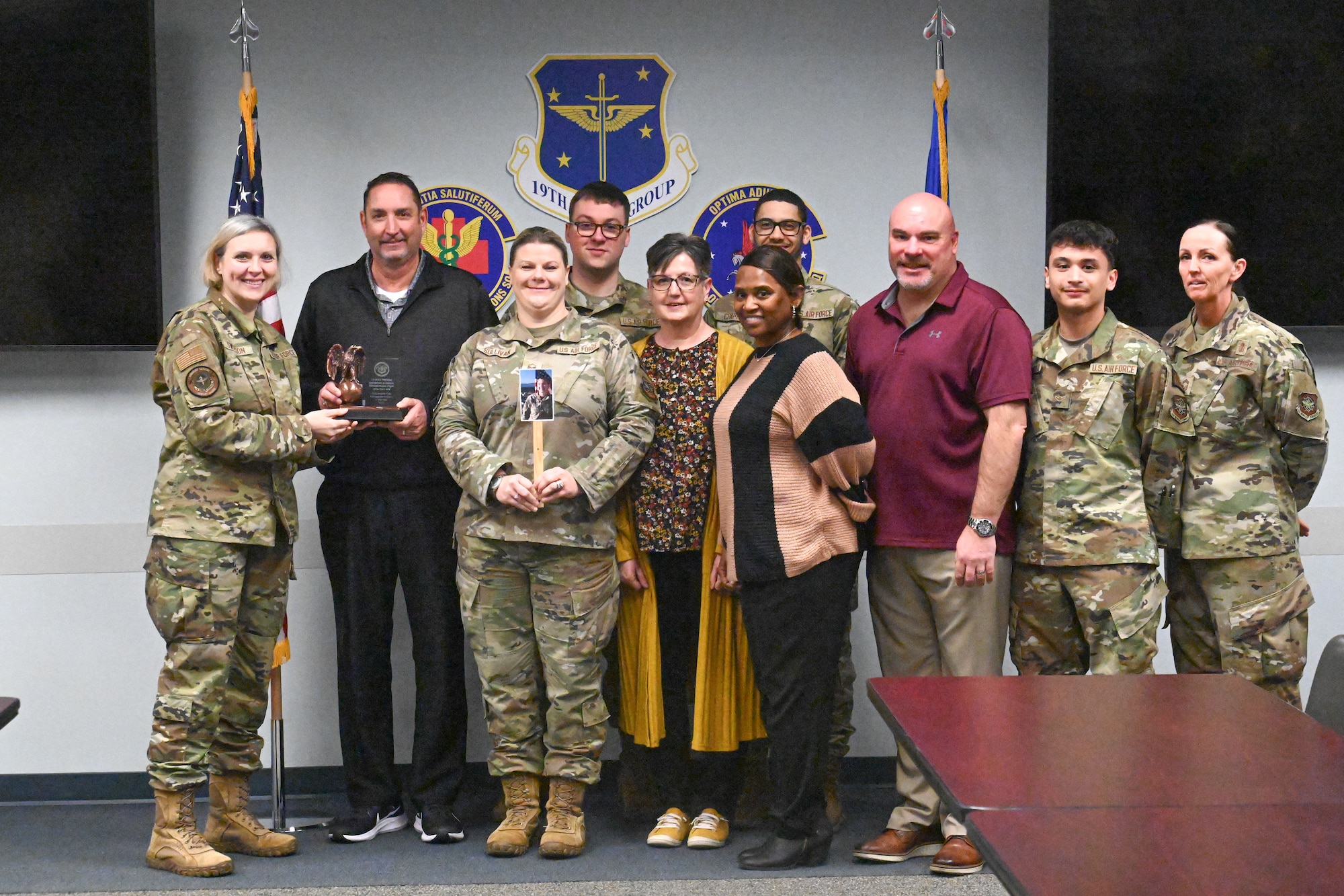 Airmen stand and pose for a photo in a medical buidling conference room.