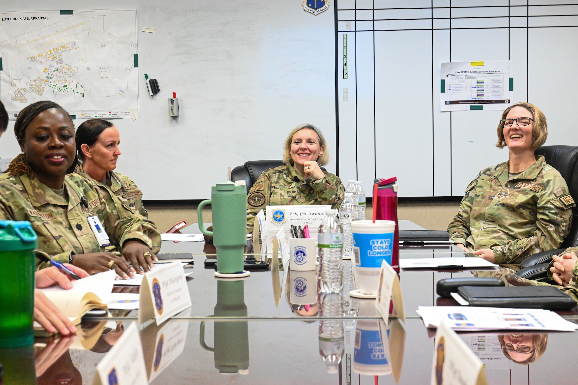 Airmen sit around a table in a conference room and laugh.