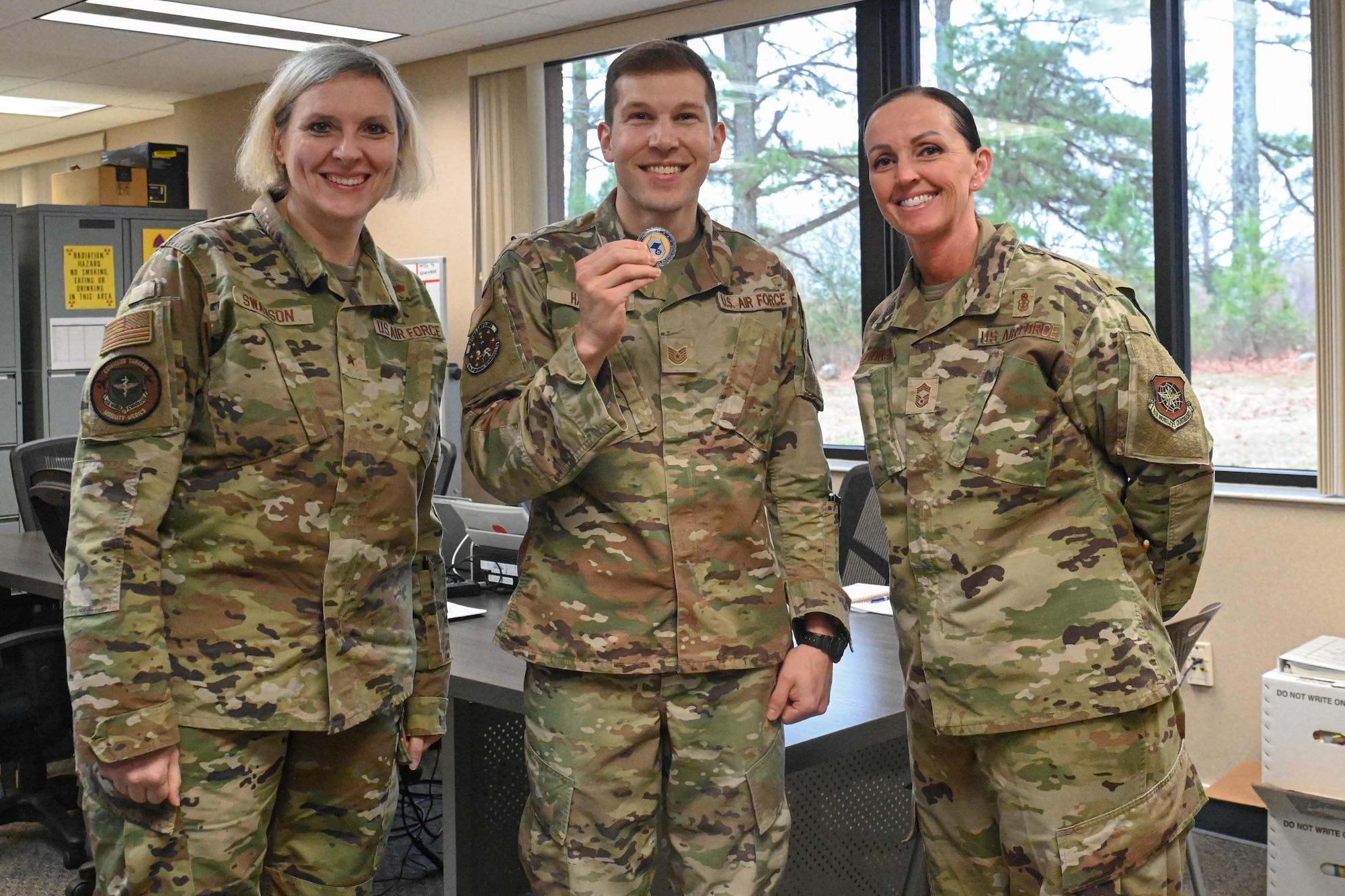 Three Airmen stand and pose for a photo as one Airman receives an award.