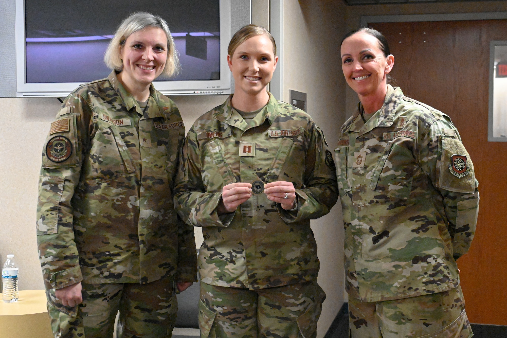 Three Airmen stand and pose for a photo as one Airman receives an award.