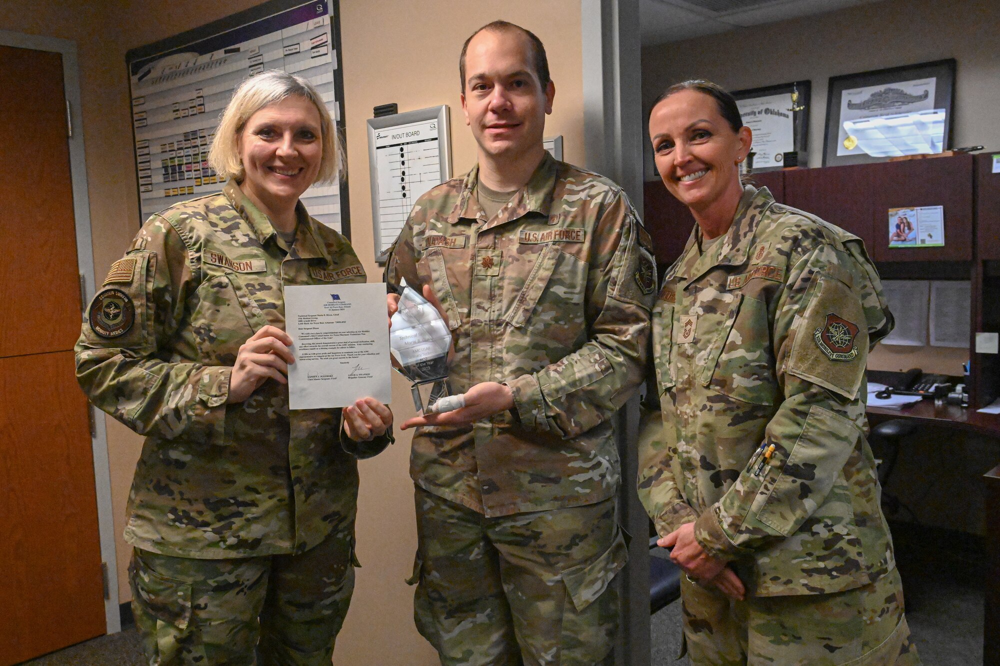 Three Airmen stand and pose for a photo as one receives an award.