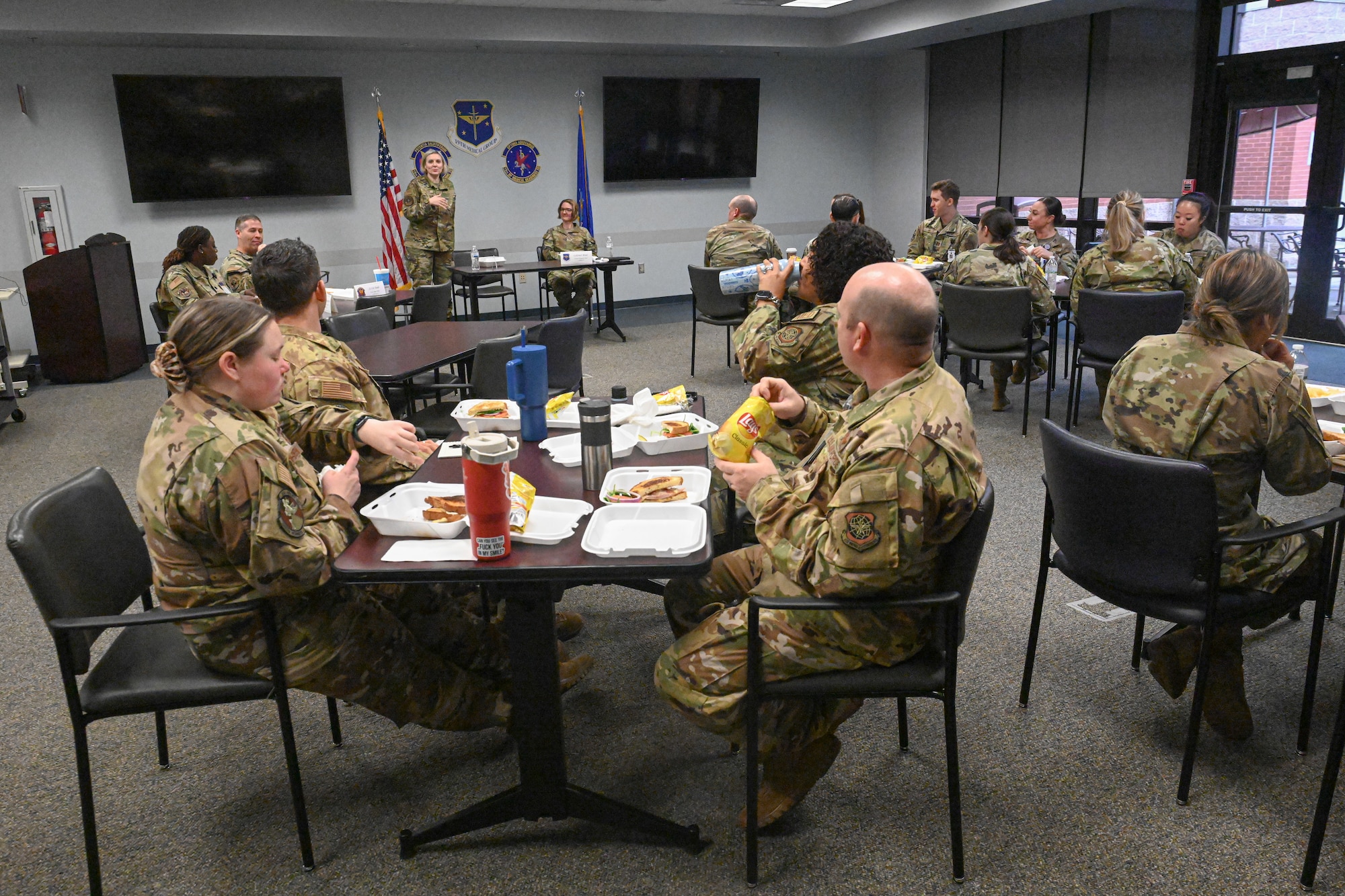 Airmen sit at tables in a conference room and talk.