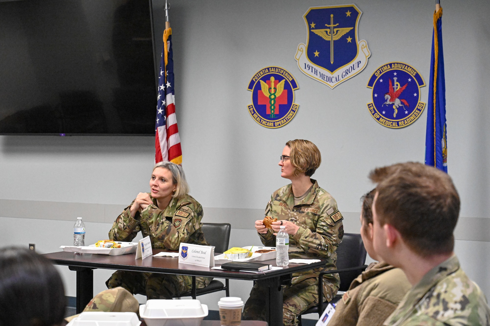 Airmen sit at tables in a conference room and talk.