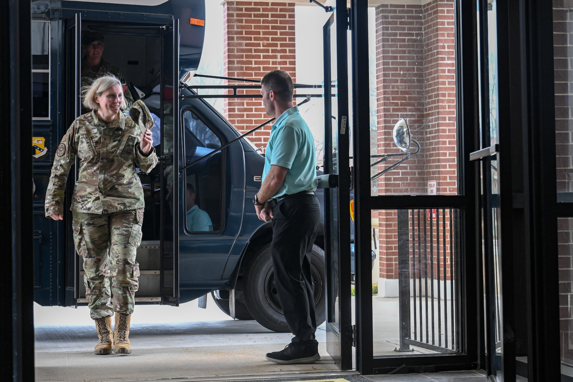 An Airman walks through a door as a man greets her.