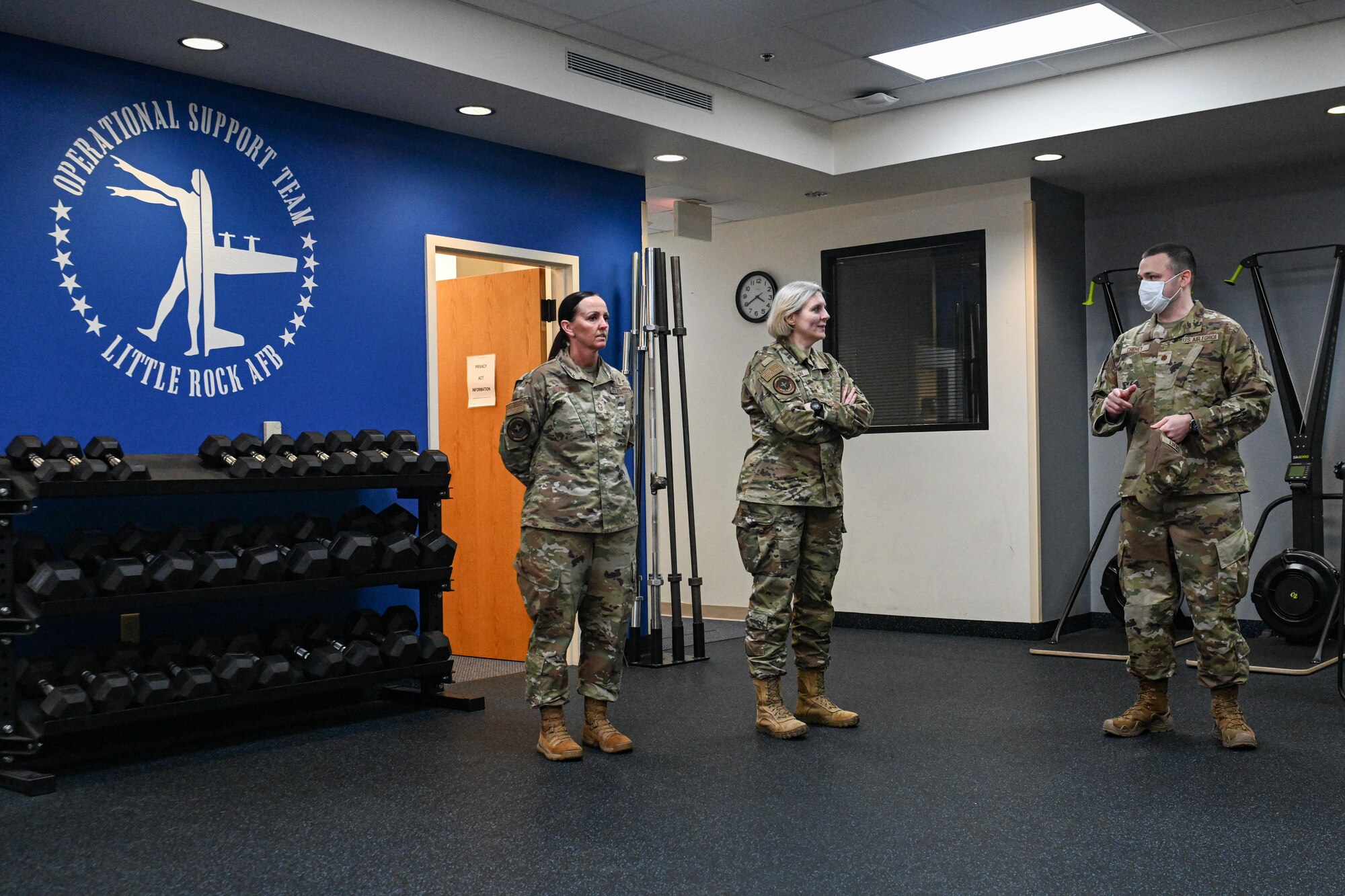 Three Airmen stand and talk in a fitness room.