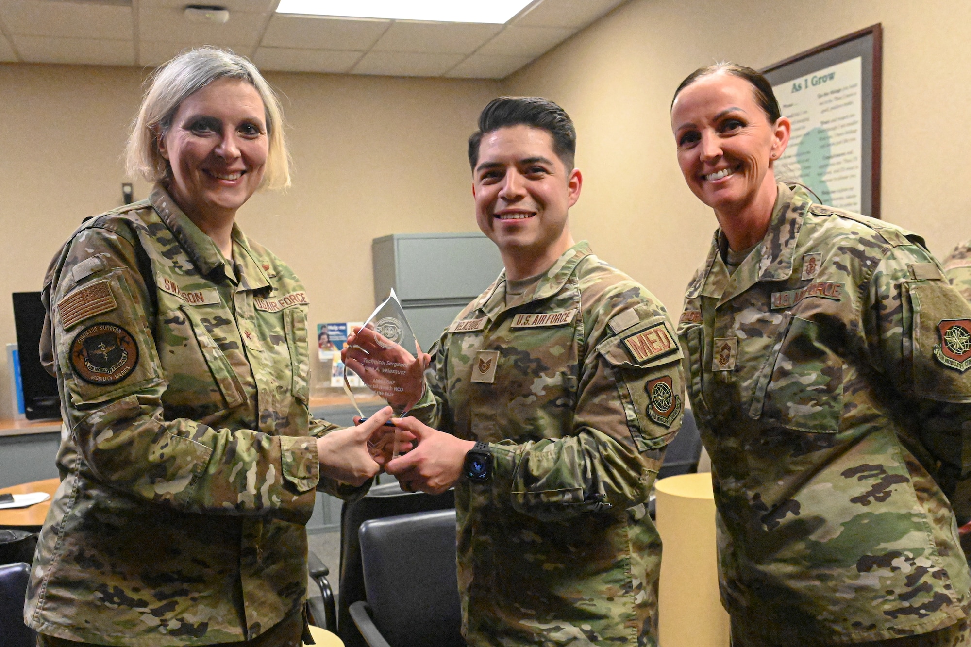 Three Airmen pose for a photo as one Airmen receives an award.