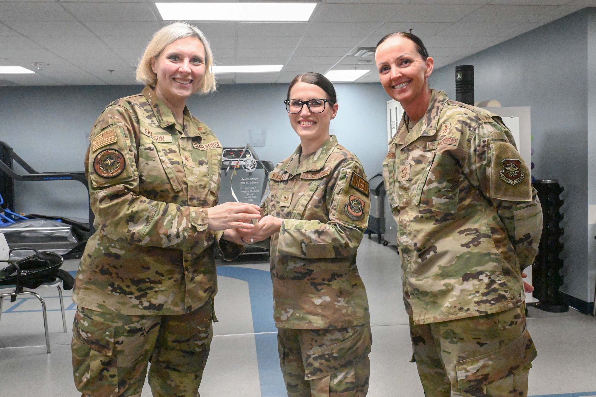 Three Airmen pose for a photo as one of the Airmen is presented an award.