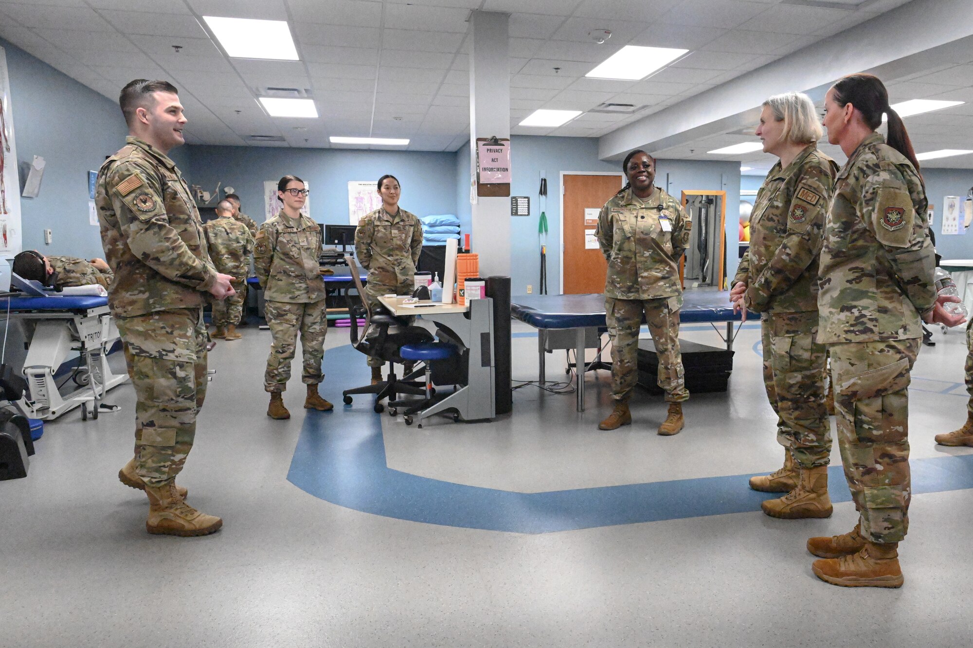 A group of Airmen stand around and have a discussion in a physical therapy room.