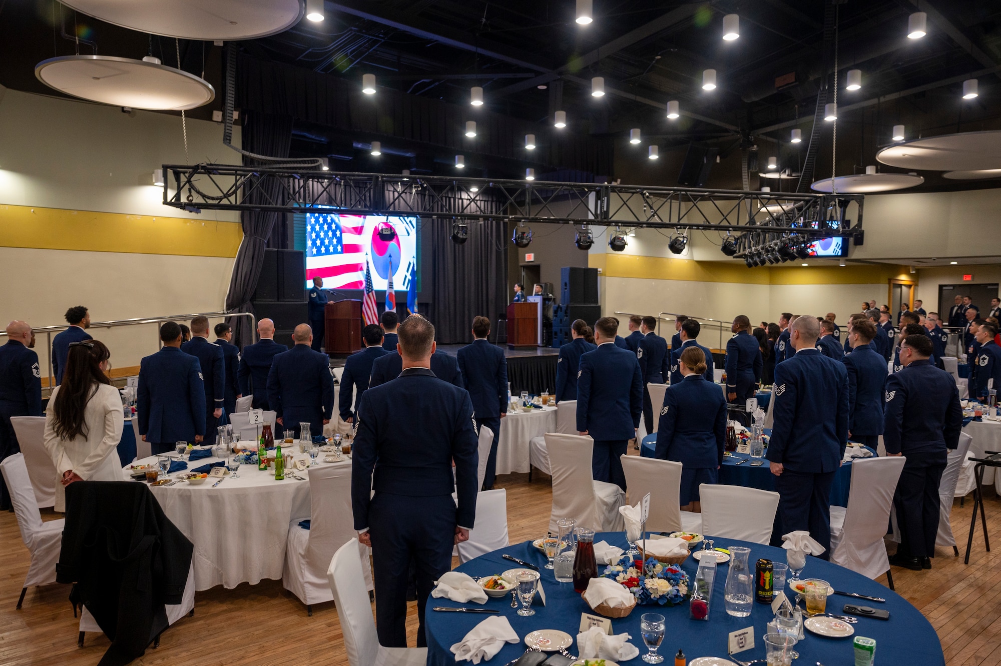 Attendants of the Airman Leadership School Class 24-A graduation stand at attention during the national anthem at Osan Air Base, Republic of Korea, Feb. 15, 2024. ALS prepares Airmen and Guardians to be adaptable and learn how to operate in complex and ambiguous environments through the application of four outcome-based objectives focusing on military culture, mission, leadership and problem-solving. (U.S. Air Force photo by Senior Airman Kaitlin Castillo)