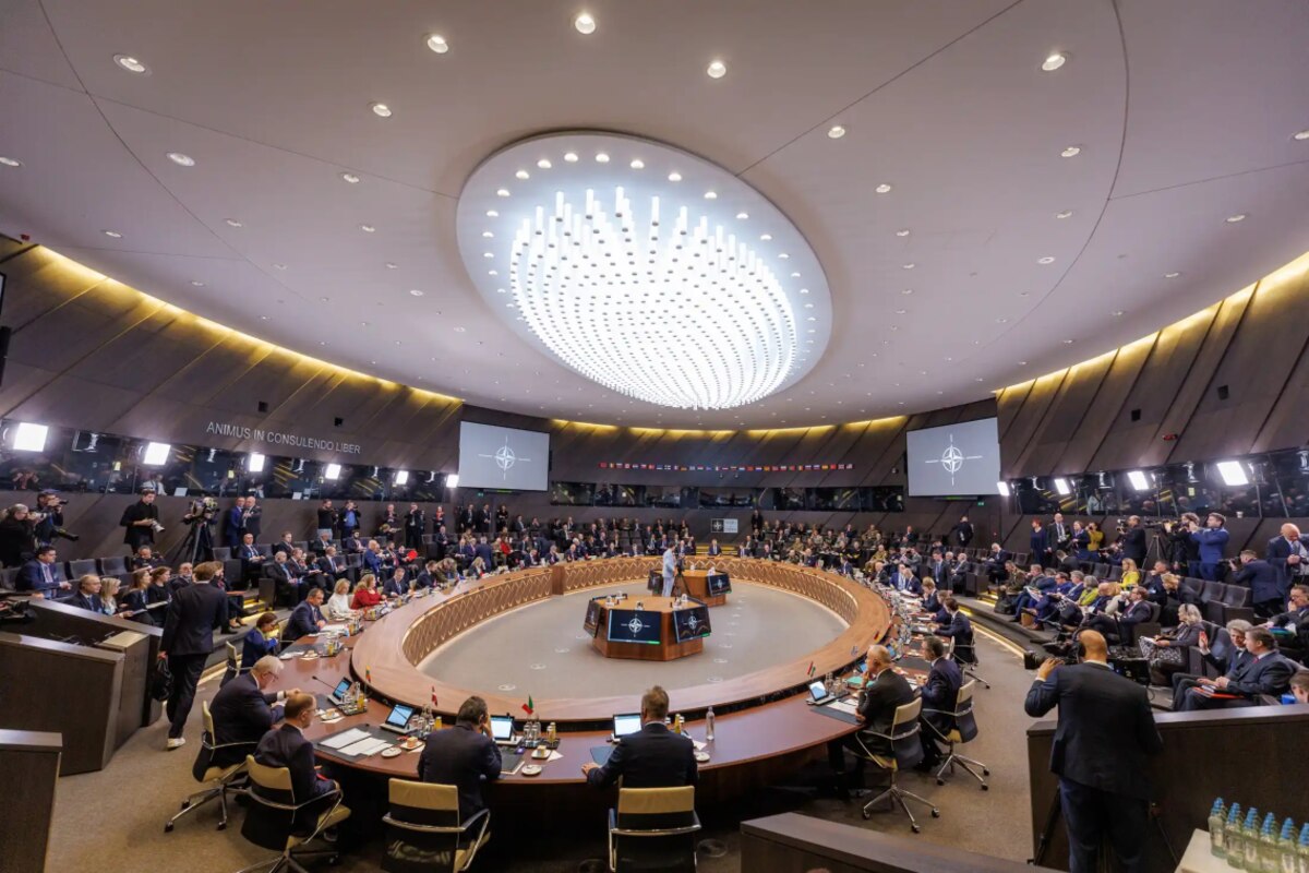 People sit around an oval table as others watch.