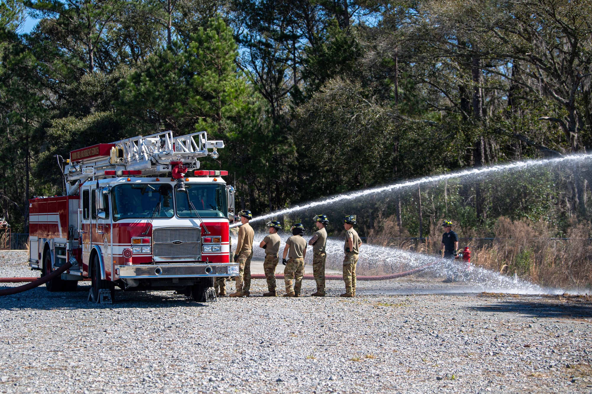 Airmen lined up watch water spray from a firetruck