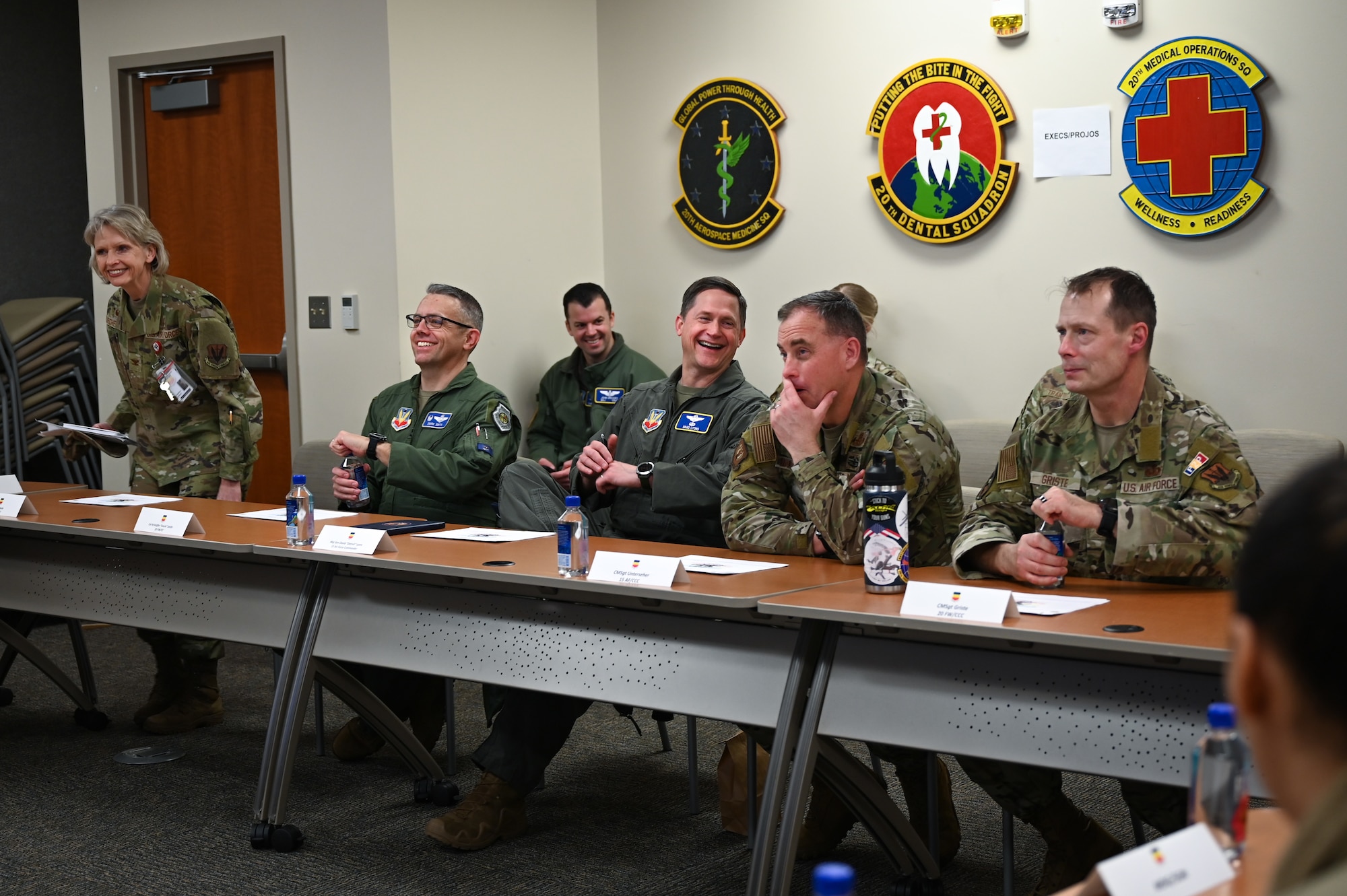 Six military personnel have a laugh while sitting at a conference table.