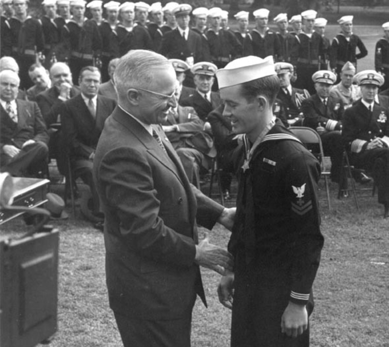 A man shakes hands with another man as others watch in the background.
