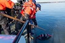 A photo of a man using a pole to hoist a simulated person out of the water.