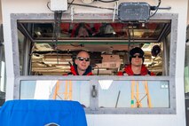 A photo of two men looking out of a boat cabin’s window.