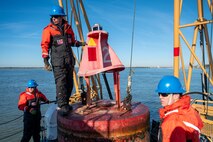 A photo of three men working on a buoy.