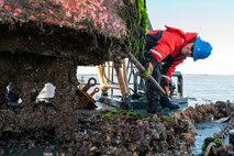 A photo of a man scraping the side of a buoy.