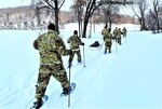 Service members wearing snowshoes and carrying ski poles traverse snow-covered hills.