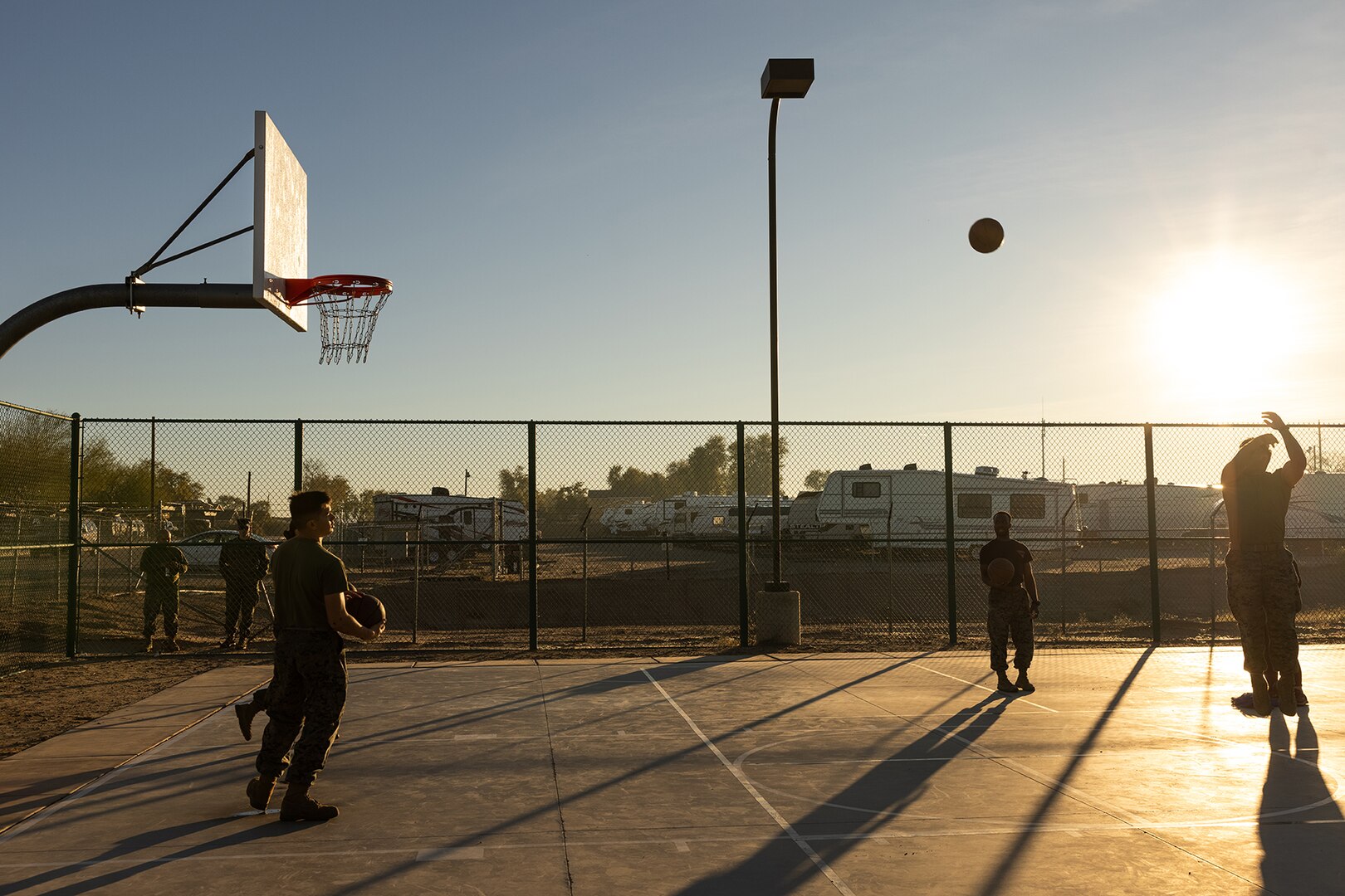 Service members play basketball on an outdoor court.