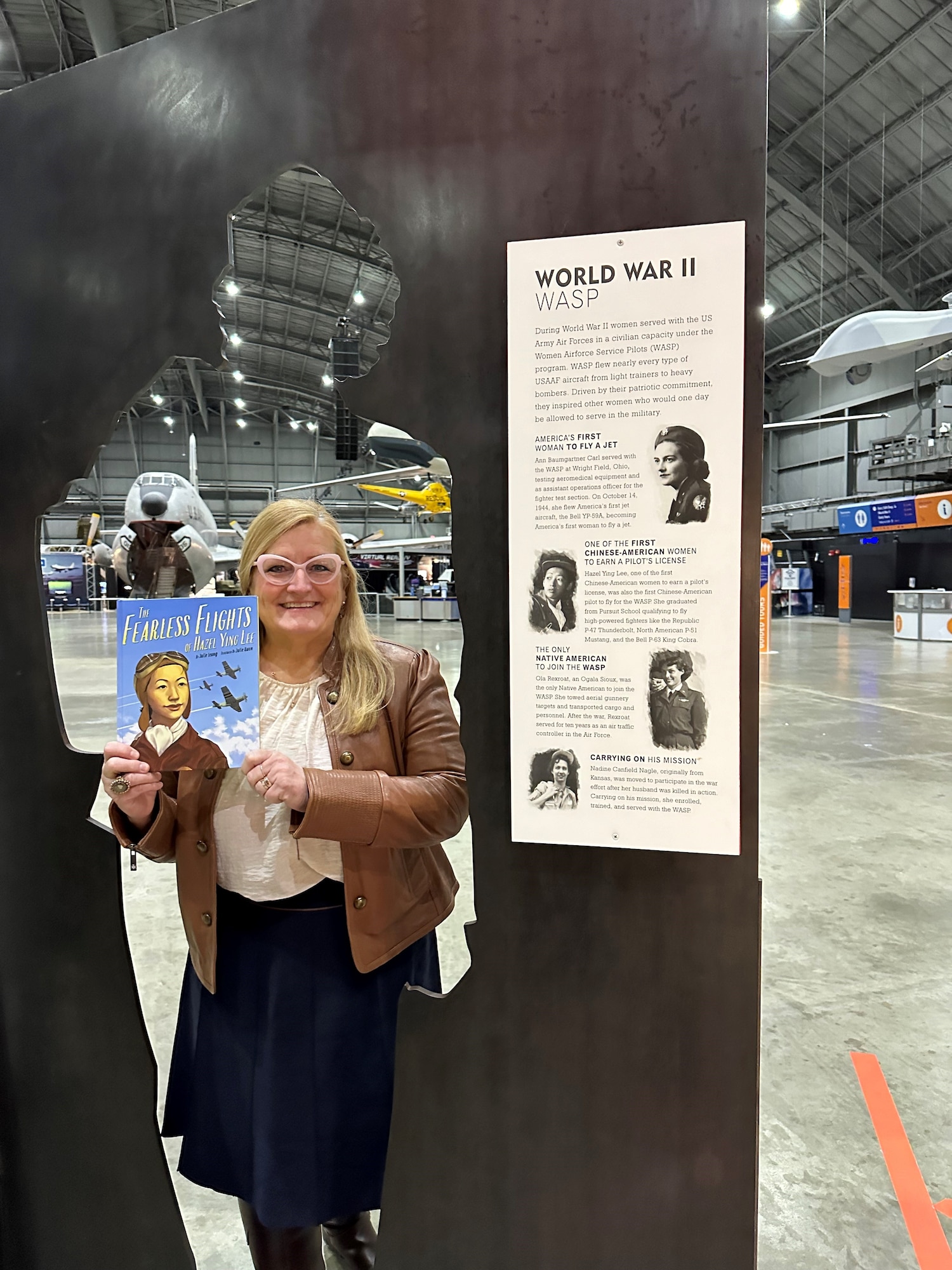 Ohio Education Association CFO Kristy Spires stands in a cut out of of a woman in the Women in the Air Force Exhibit, holding the book Fearless Flights.