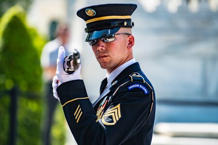 A soldier with sunglasses on is looking sideways while inspecting a rifle that has a bayonet attached.