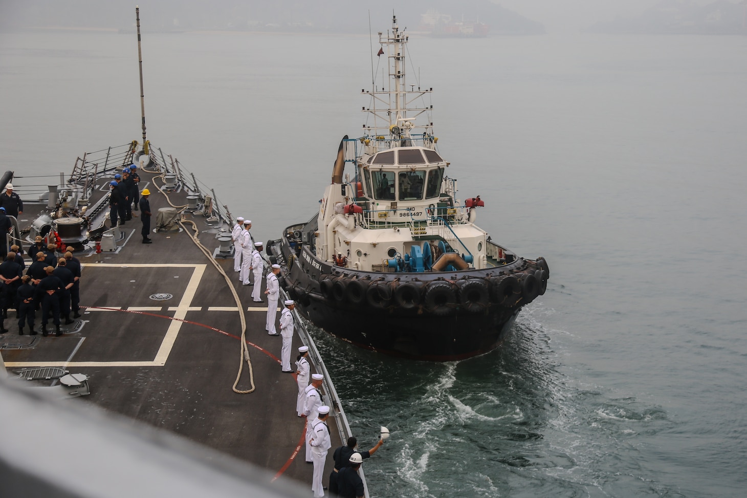 First Lieutenant, LTJG Ezra Haddock, from San Diego, Calif., waves in forward tug while pulling into port in support of Exercise Milan 2024 onboard the forecastle of the arleigh-burke class guided missile destroyer USS Halsey (DDG-97), Feb. 18, 2024.