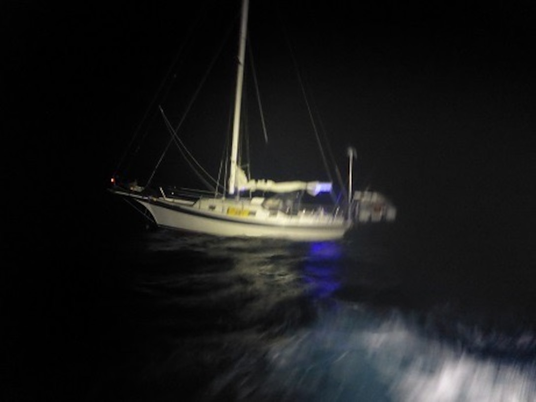 White sailing vessel in heavy seas at night with spotlight illuminating middle section.