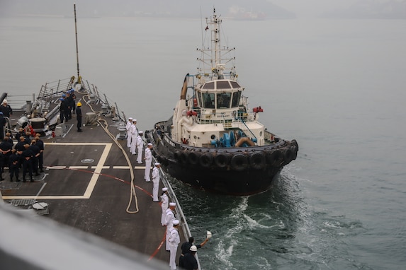 First Lieutenant, LTJG Ezra Haddock, from San Diego, Calif., waves in forward tug while pulling into port in support of Exercise Milan 2024 onboard the forecastle of the arleigh-burke class guided missile destroyer USS Halsey (DDG-97), Feb. 18, 2024.