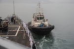 VISHAKAPATNAM, India (Feb. 18, 2024) First Lieutenant, LTJG Ezra Haddock, from San Diego, Calif., waves in forward tug while pulling into port in support of Exercise Milan 2024 onboard the forecastle of the arleigh-burke class guided missile destroyer USS Halsey (DDG-97), Feb. 18, 2024. U.S. Navy photo by ENS Chloe VonderLinden.