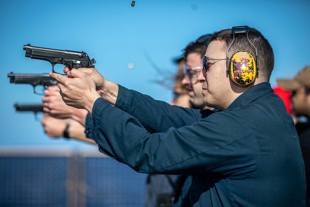 Three sailors shown in profile fire pistols on a ship's flight deck.