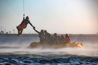A Sailor lowers from a helicopter to a life raft during maritime recovery training in San Diego Bay.