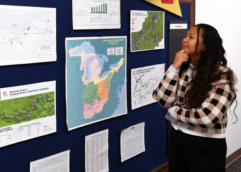 Woman stands near pin board looking at maps.