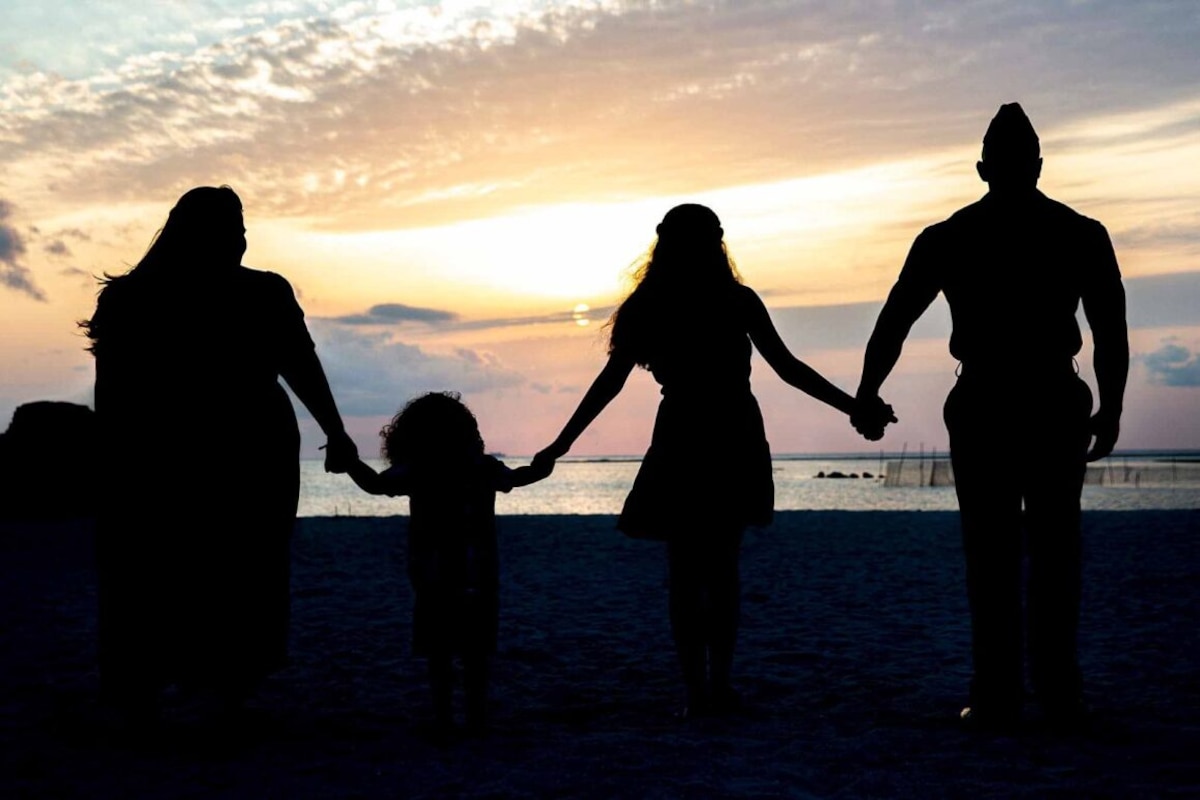 Four people in silhouette hold hands as they look at the setting sun.
