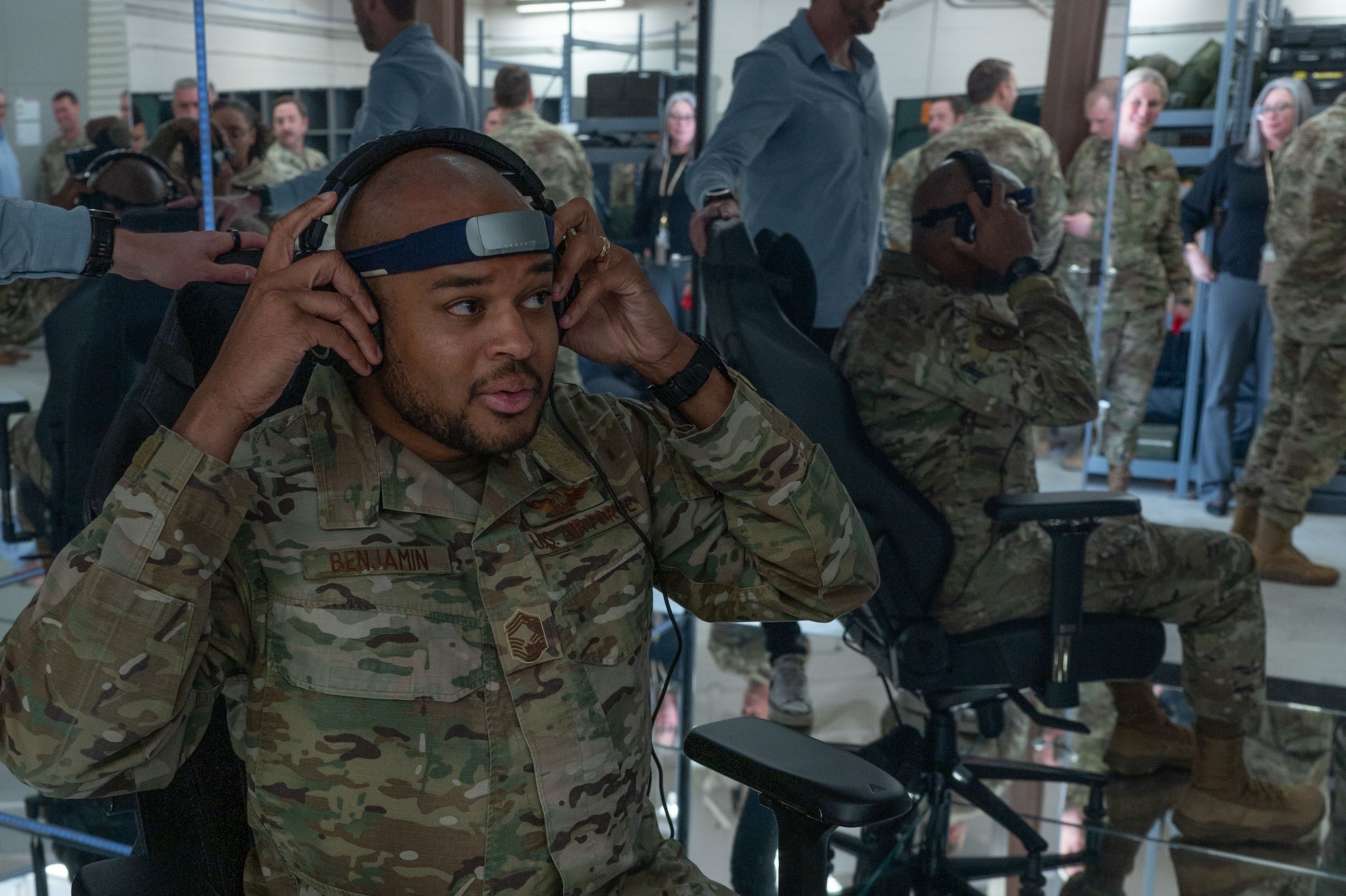 A man in military uniform sits on a chair inside a mirrored room, putting on a headset.