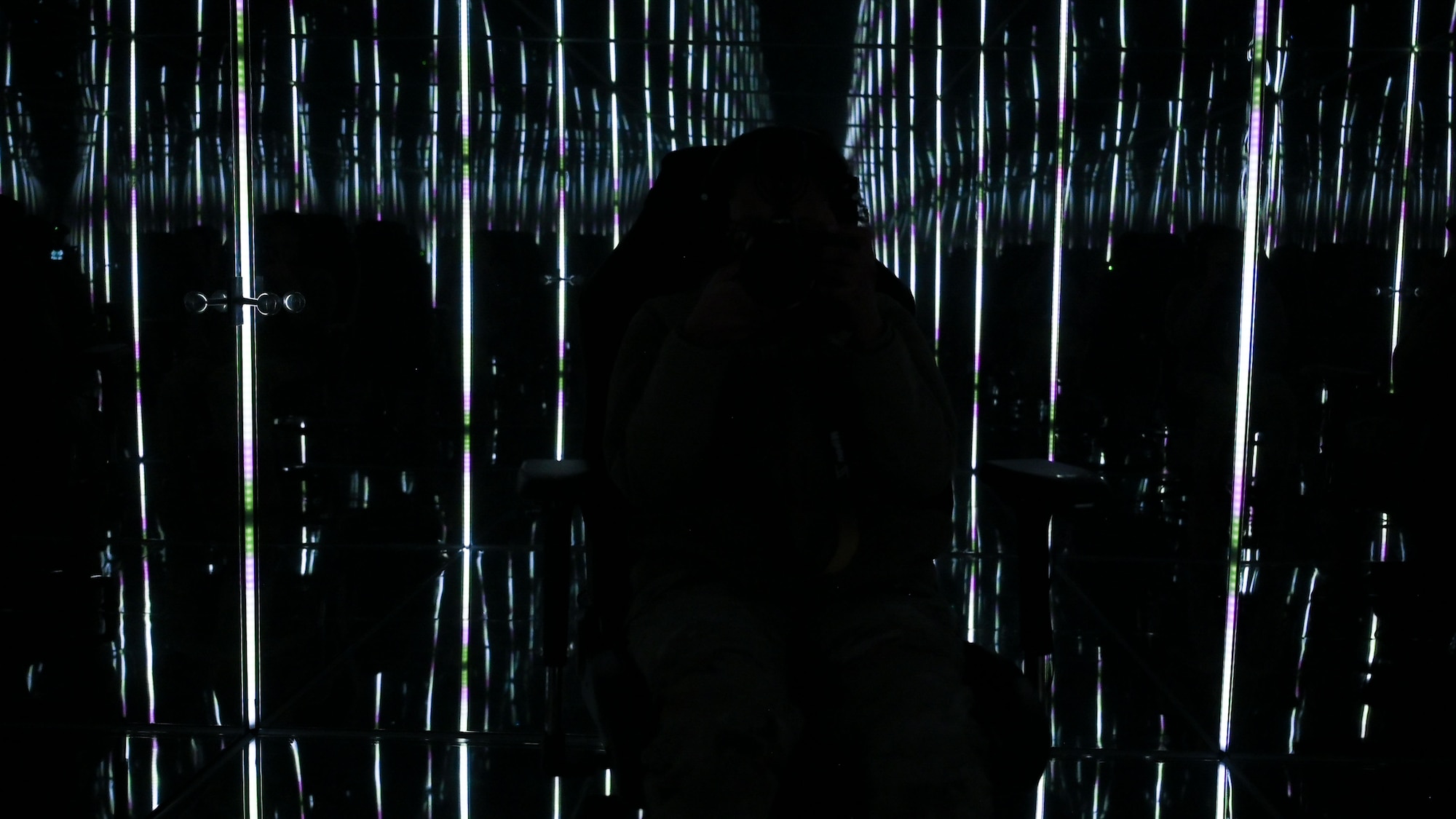 A person sits in a dark mirrored room with various lights reflecting.