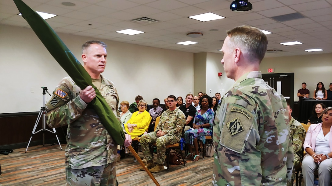 Brig. Gen. Daniel and Colonel Charles Decker both dressed in camouflage uniforms, standing in front of a seated group of people.