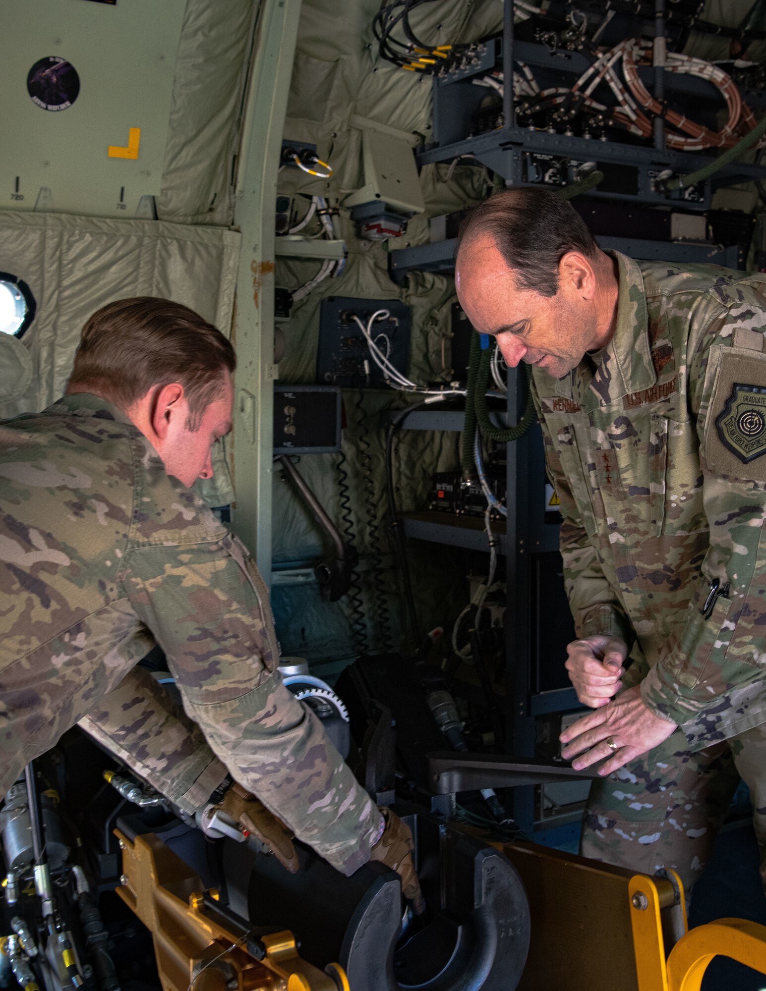 Two men in military uniform load a cannon inside a military aircraft.