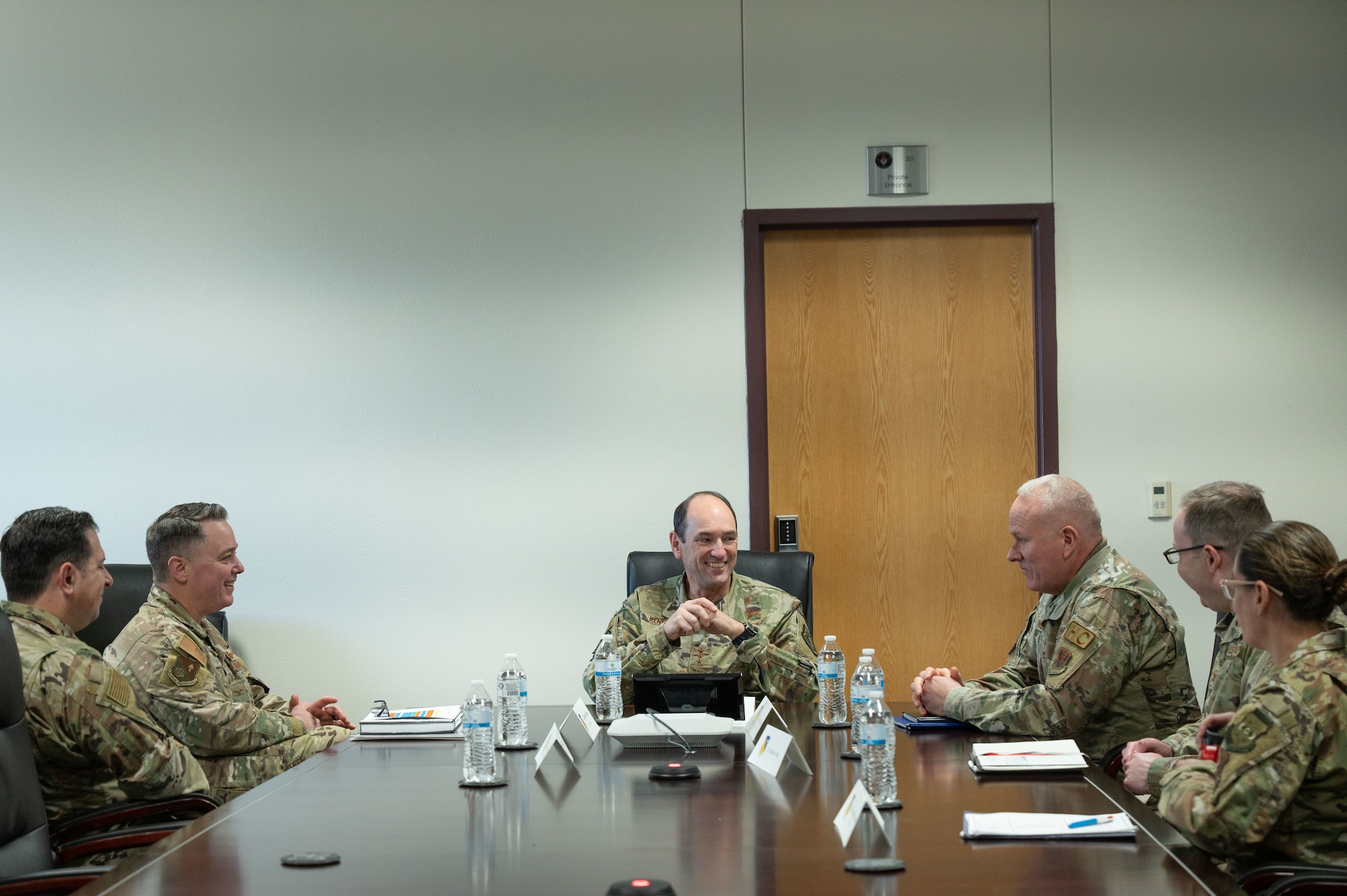 A group of men and women in military uniform sit around a conference table smiling and talking.