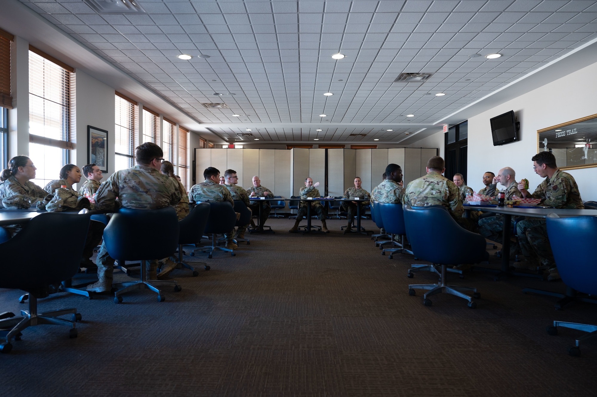 A group of men and women in military uniform sit around tables in a room.